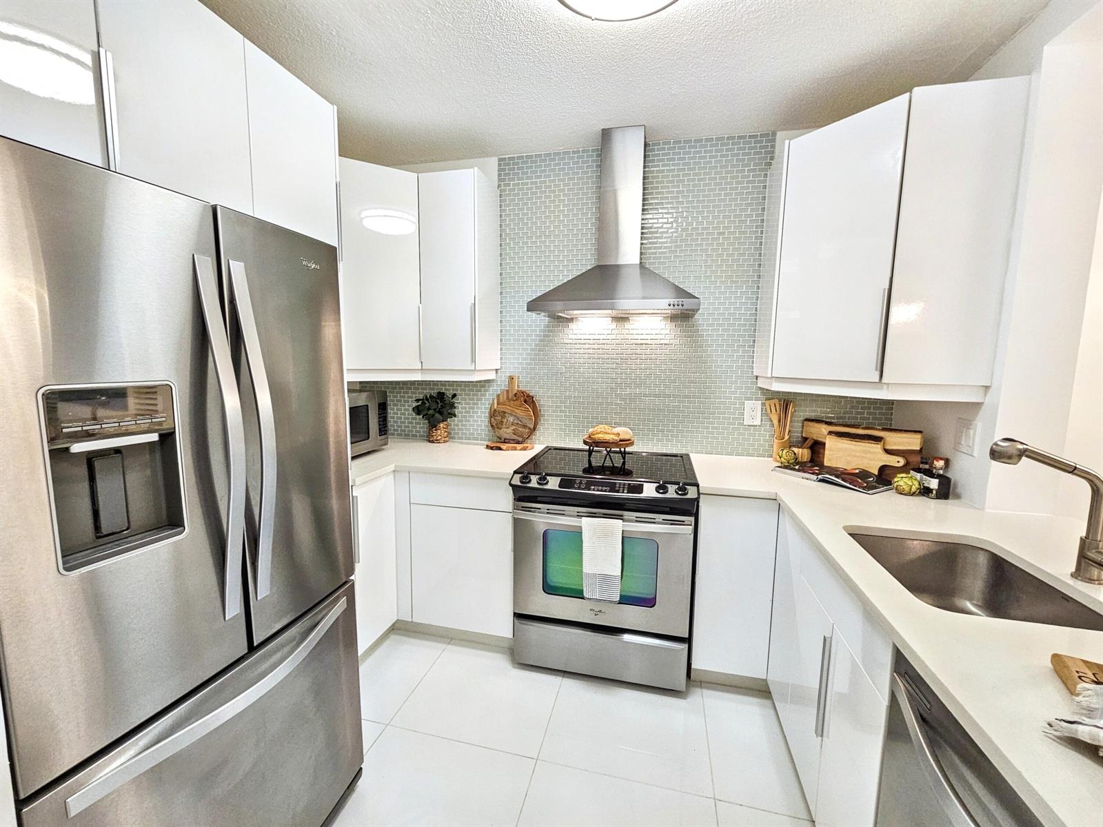 A modern kitchen features white cabinets, stainless steel appliances, and a light green tiled backsplash — 6530 N Ocean Boulevard # 1080, Ocean Ridge FL 33435, OCEAN RIDGE, FL