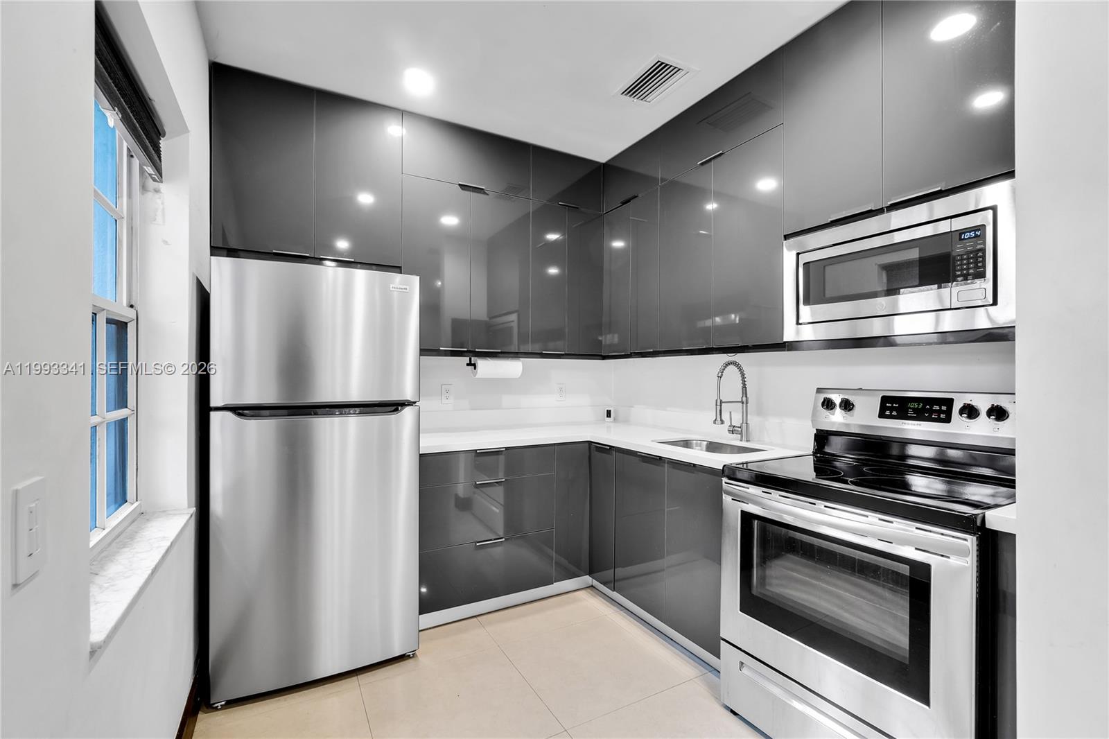 A modern kitchen features glossy gray cabinets, stainless steel appliances, and white countertops — 8335 E Crespi Blvd # 4, Miami Beach FL 33141, MIAMI BEACH, FL