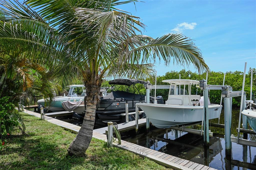 A palm tree stands beside a wooden dock with several boats moored in a canal — 6817 BAYSHORE ROAD, PALMETTO, FL