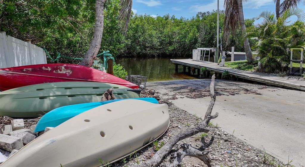 A concrete boat ramp leads to a wooden dock surrounded by kayaks and lush vegetation — 6817 BAYSHORE ROAD, PALMETTO, FL
