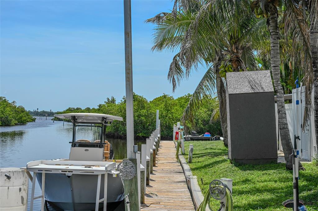 A boat is docked at a wooden pier next to a grassy yard and palm trees — 6817 BAYSHORE ROAD, PALMETTO, FL