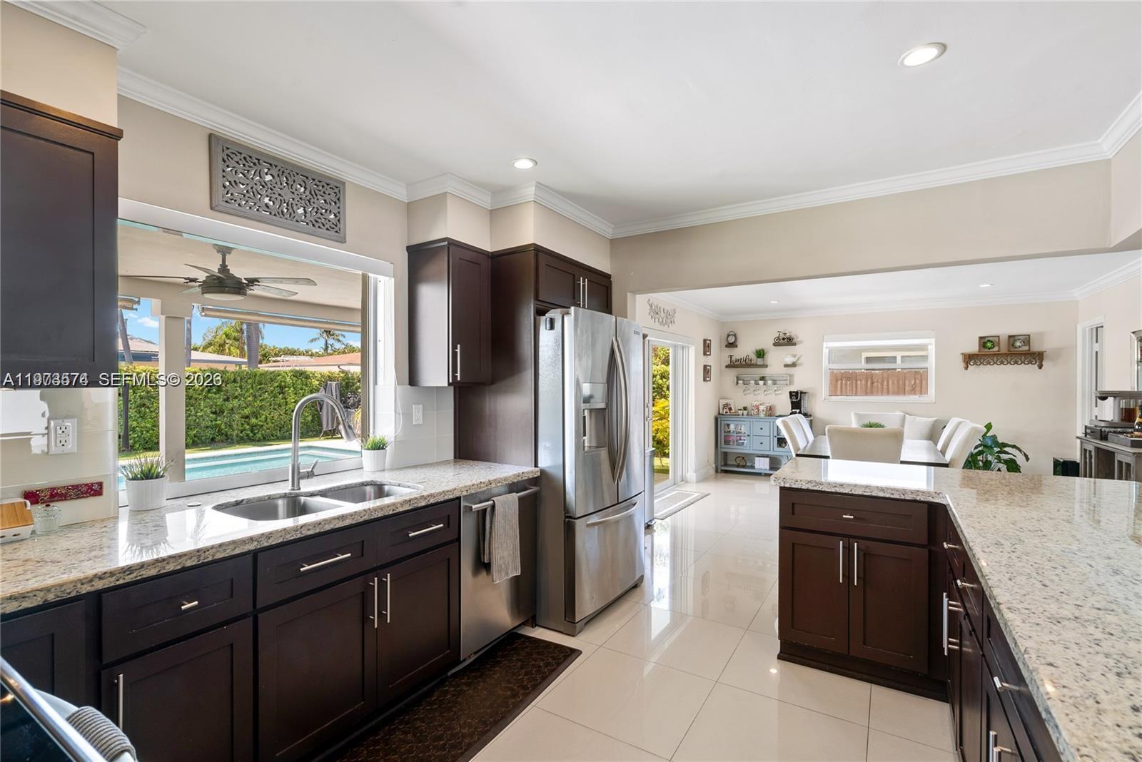 A kitchen with dark wood cabinets, granite countertops, and stainless steel appliances overlooks a pool — 19900 SW 83rd Ave, Cutler Bay FL 33189, CUTLER BAY, FL