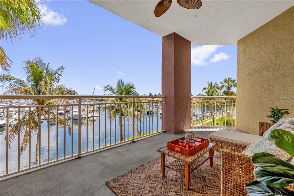 A covered balcony with wicker furniture overlooks a marina with boats and palm trees — 606 RIVIERA DUNES WAY UNIT 207, PALMETTO, FL