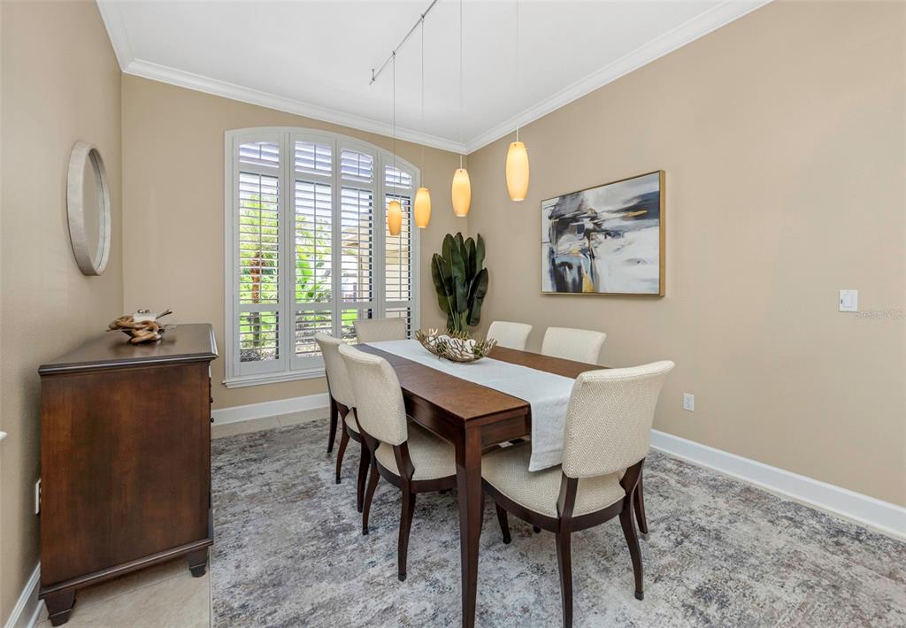 A dining room features a wooden table, six upholstered chairs, pendant lights, and arched shutters — 3675 JANUS WAY, PALM HARBOR, FL