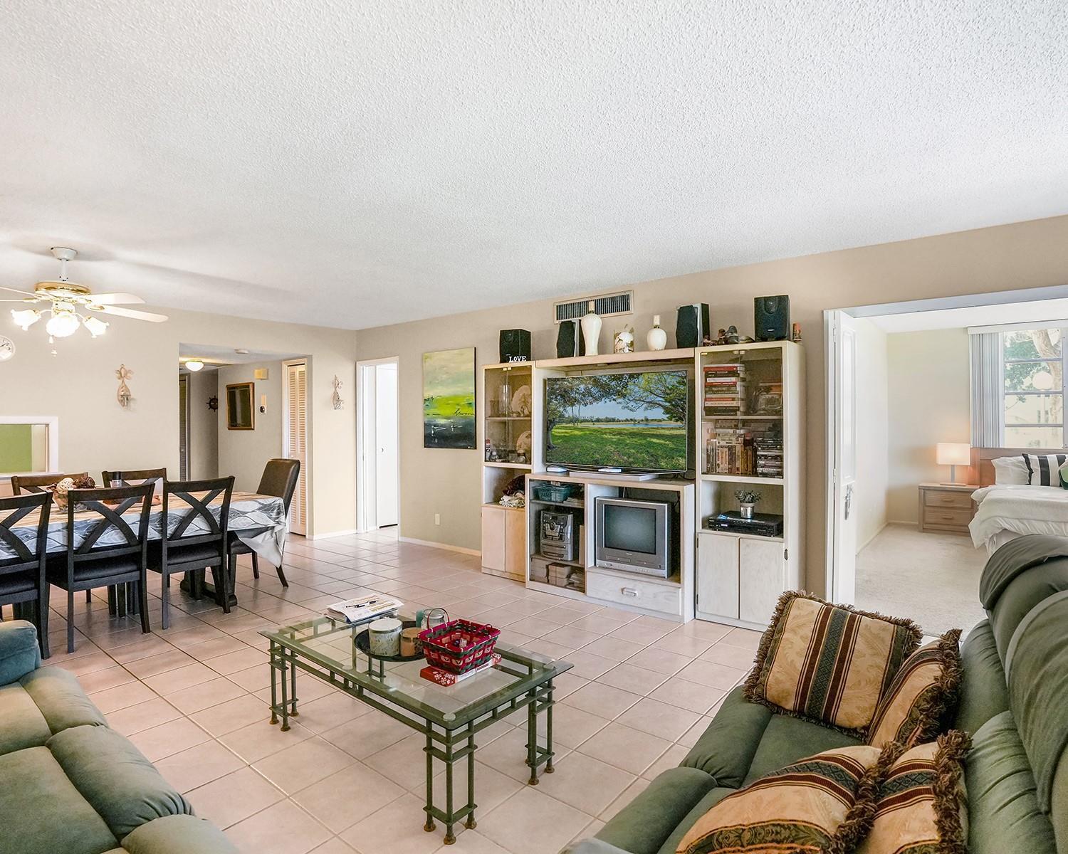 A living room with tile floors, a large entertainment center, and an adjacent dining area — 3090 N Course Drive # 112, Pompano Beach FL 33069, POMPANO BEACH, FL