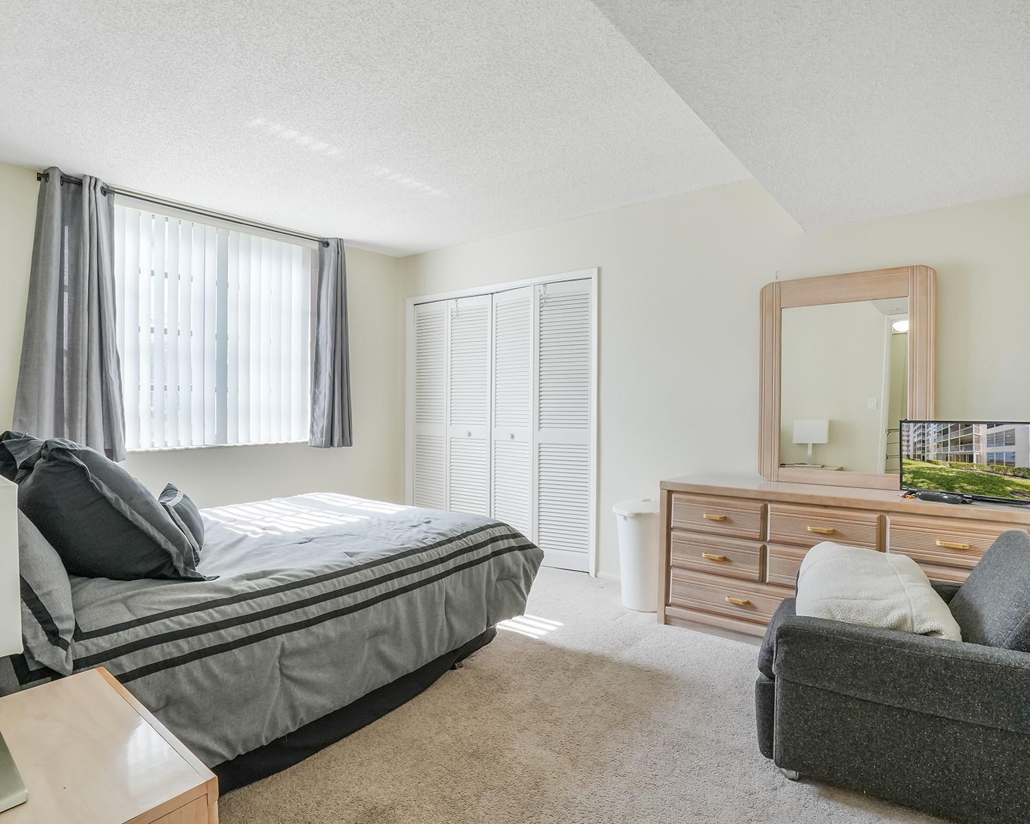 A bedroom features a bed, a dresser with a mirror, a chair, and closet doors — 3090 N Course Drive # 112, Pompano Beach FL 33069, POMPANO BEACH, FL
