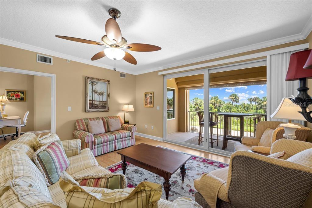 A living room features plaid furniture, a ceiling fan, and a balcony with outdoor seating — 80 SURFVIEW DRIVE UNIT 118, PALM COAST, FL