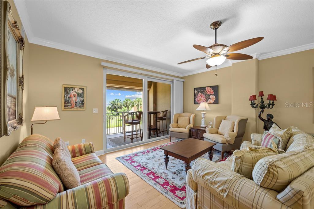 A living room features a striped sofa, patterned armchairs, a ceiling fan, and a balcony view — 80 SURFVIEW DRIVE UNIT 118, PALM COAST, FL
