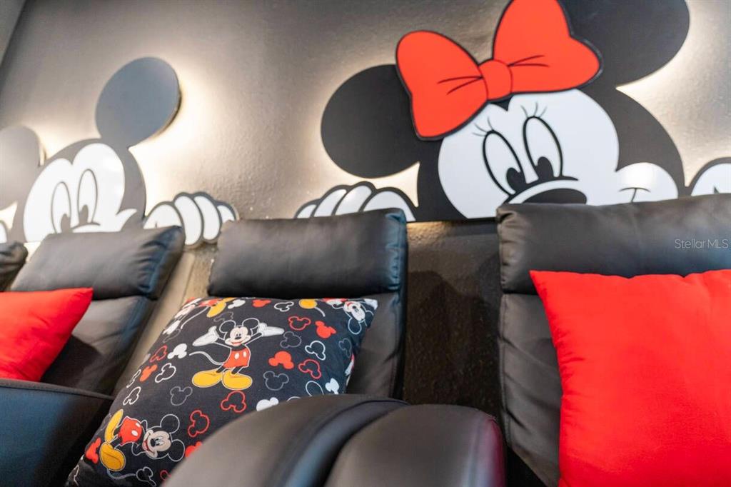 A home theater room features black leather recliners with Mickey Mouse-themed pillows and wall art — 4541 TARGET BOULEVARD, KISSIMMEE, FL