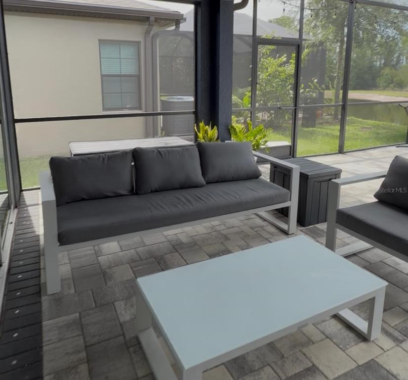 A screened-in patio features a modern gray sofa, a matching coffee table, and paver flooring — 18071 AERO AVENUE, LAND O LAKES, FL