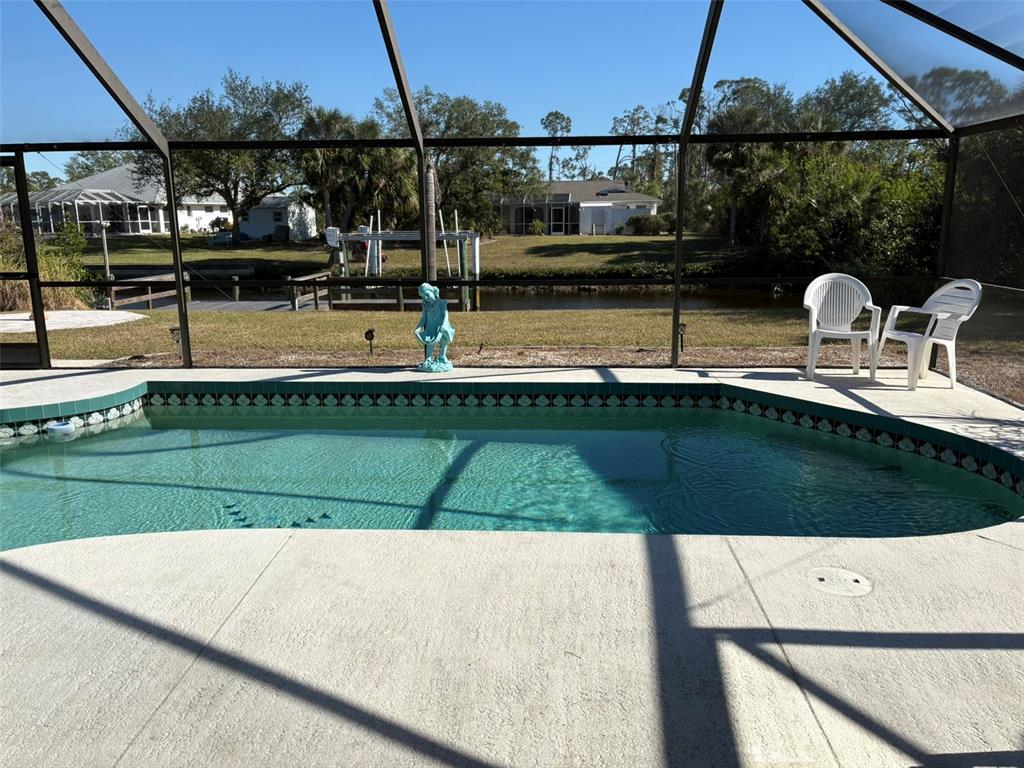 A swimming pool sits inside a screened-in lanai overlooking a canal and neighboring houses — 17377 LAKE WORTH BOULEVARD, PORT CHARLOTTE, FL