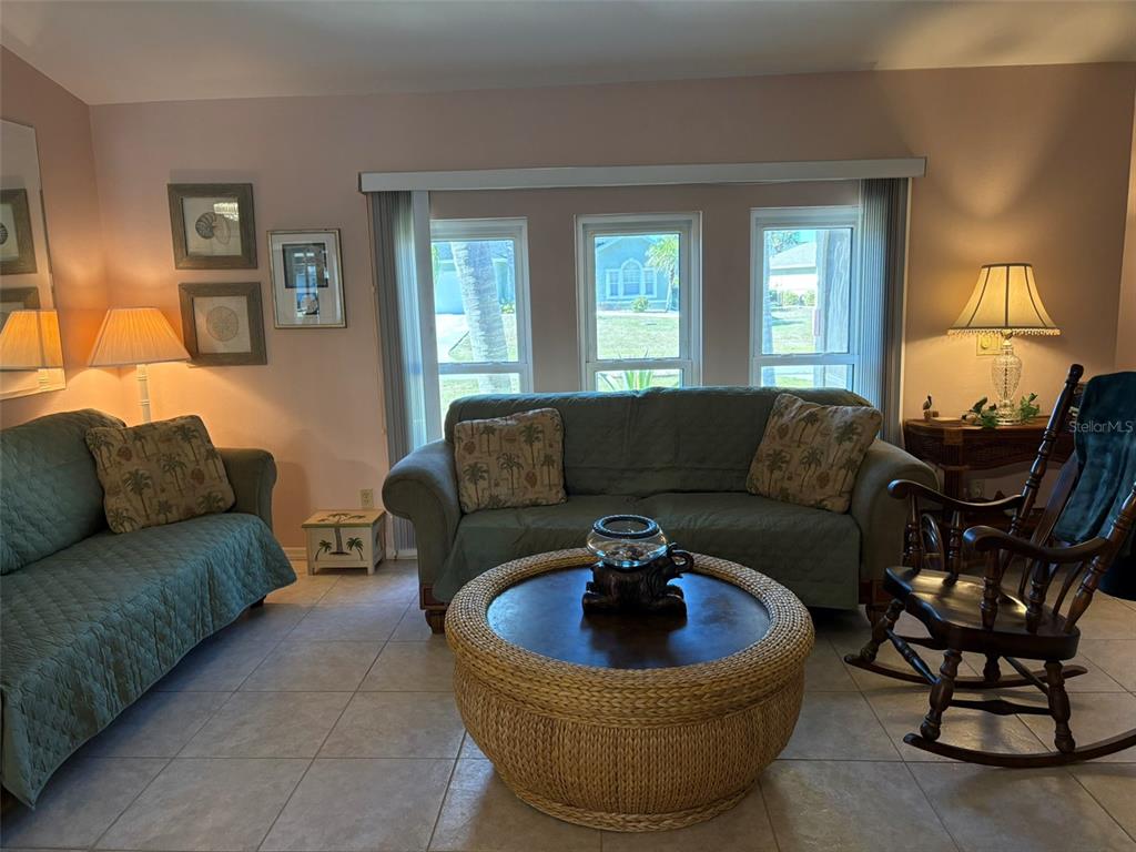 A living room features two green sofas, a round wicker coffee table, and a rocking chair — 17377 LAKE WORTH BOULEVARD, PORT CHARLOTTE, FL