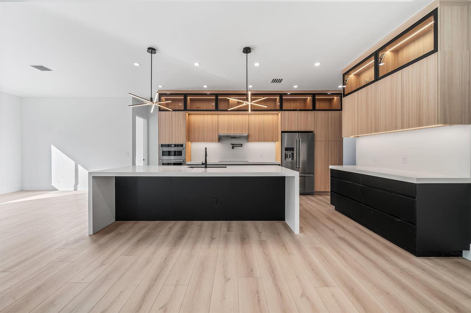 A modern kitchen features a large white island, black cabinetry, and light wood-toned upper cabinets — 18651 49th Street, Loxahatchee FL 33470, LOXAHATCHEE, FL