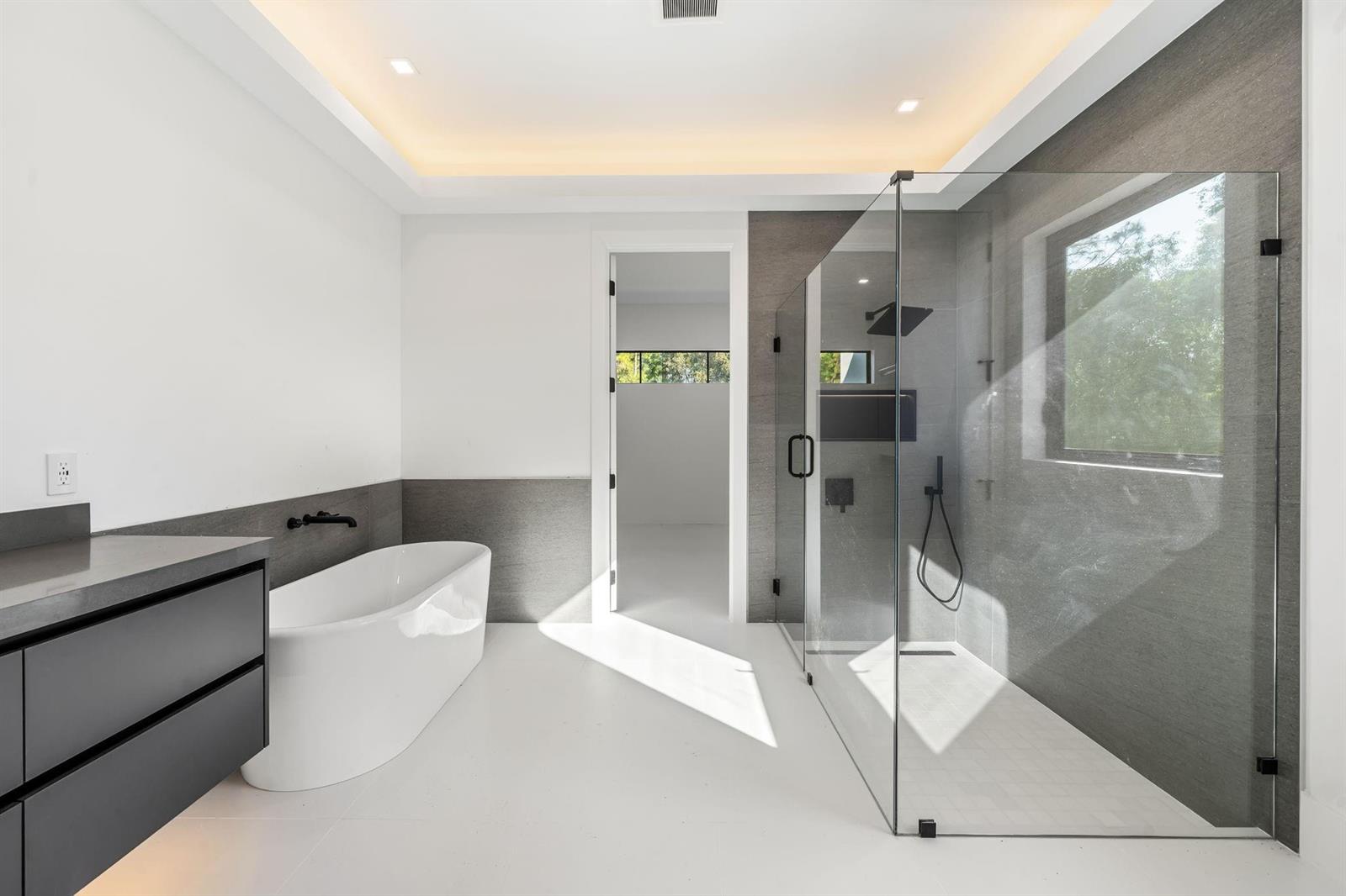A modern bathroom features a freestanding tub, a glass-enclosed shower, and dark gray tile accents — 18651 49th Street, Loxahatchee FL 33470, LOXAHATCHEE, FL