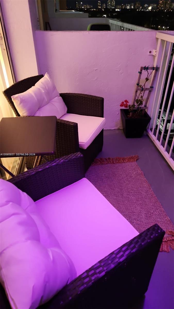 A balcony features two wicker chairs with white cushions, a small table, and a potted plant — 2000 NE 135th St # 806, North Miami FL 33181, NORTH MIAMI, FL