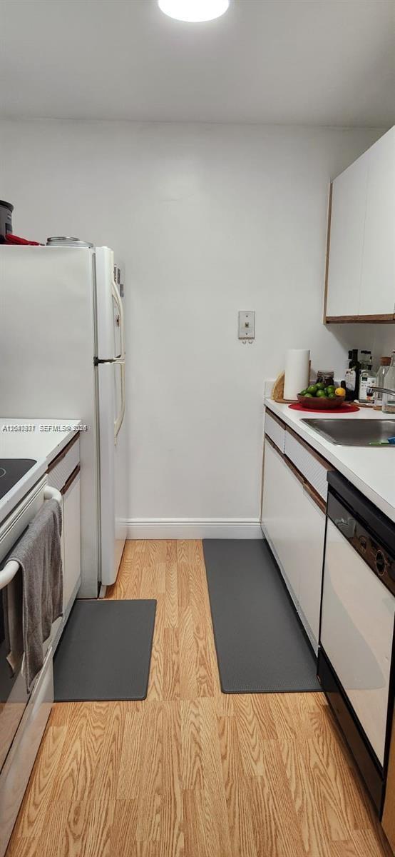A narrow galley kitchen features white cabinets, a white refrigerator, and light wood flooring — 2000 NE 135th St # 806, North Miami FL 33181, NORTH MIAMI, FL