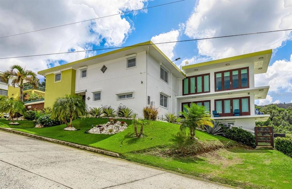 A two-story white house with lime green accents sits on a sloped, grassy residential lot — Calle 2 CARRETERA OESTE 169 UNIT 169, LUQUILLO, PR