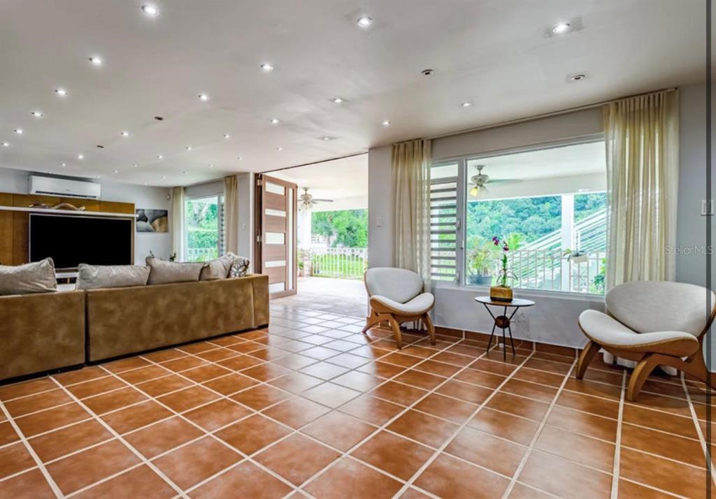 A living room with brown tile floors, a large sofa, and a view of a patio — Calle 2 CARRETERA OESTE 169 UNIT 169, LUQUILLO, PR
