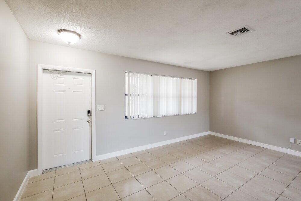 An empty room with light gray walls, beige tile flooring, a white door, and blinds — PEMBROKE PINES, FL