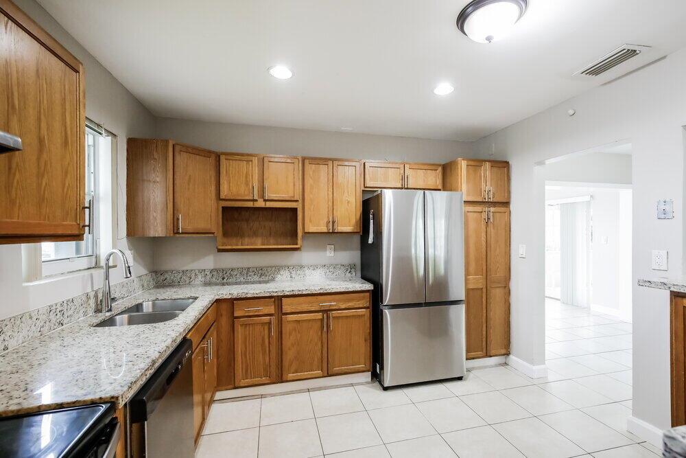 A kitchen with wood cabinets, granite countertops, stainless steel appliances, and light tile flooring — PEMBROKE PINES, FL
