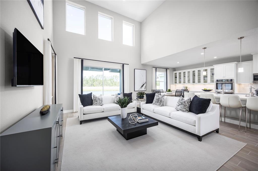 A bright, open-concept living room features high ceilings, white sofas, and an adjacent kitchen — 117 VENETIAN PALMS BOULEVARD, NEW SMYRNA BEACH, FL