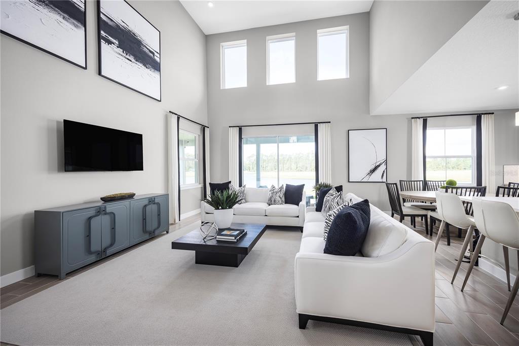 A bright, open-concept living room features high ceilings, a white sofa, and a dining area — 117 VENETIAN PALMS BOULEVARD, NEW SMYRNA BEACH, FL