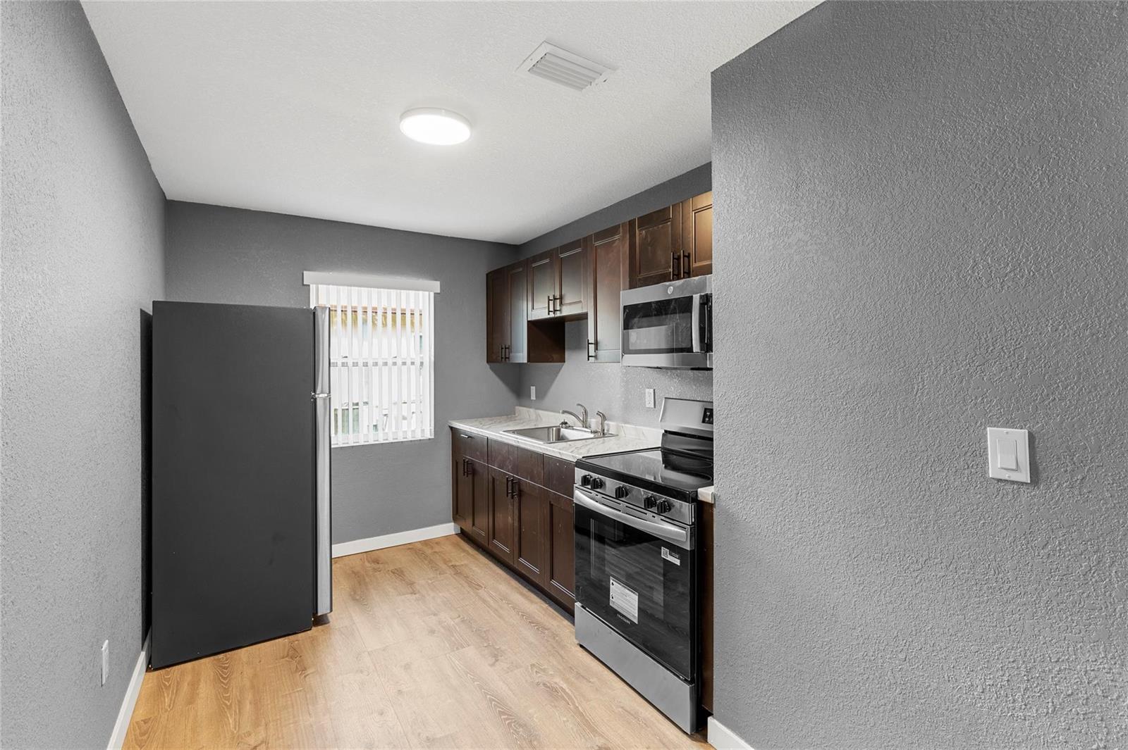 A kitchen features dark wood cabinets, stainless steel appliances, grey walls, and light wood flooring — 233 NW 12th Court, Pompano Beach FL 33060, POMPANO BEACH, FL