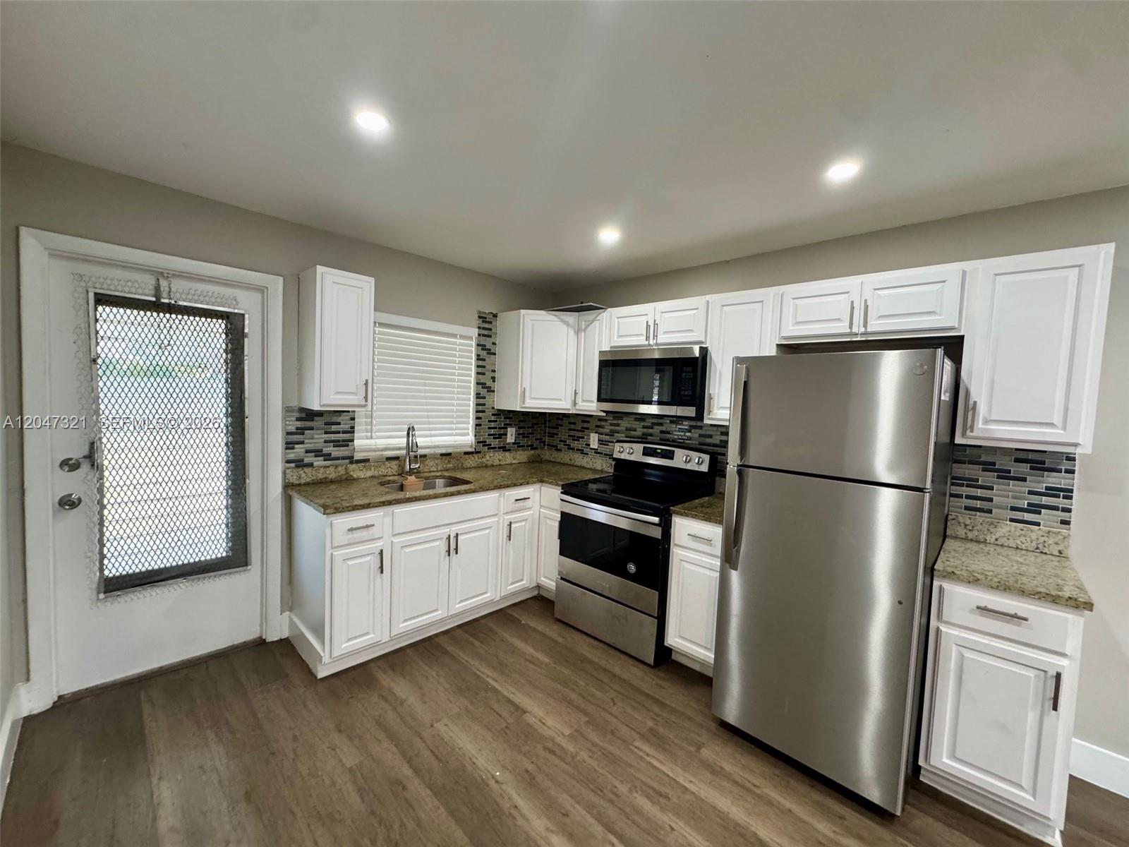 A kitchen features white cabinets, stainless steel appliances, granite countertops, and a tile backsplash — 5410 NW 16th St # 1, Lauderhill FL 33313, LAUDERHILL, FL
