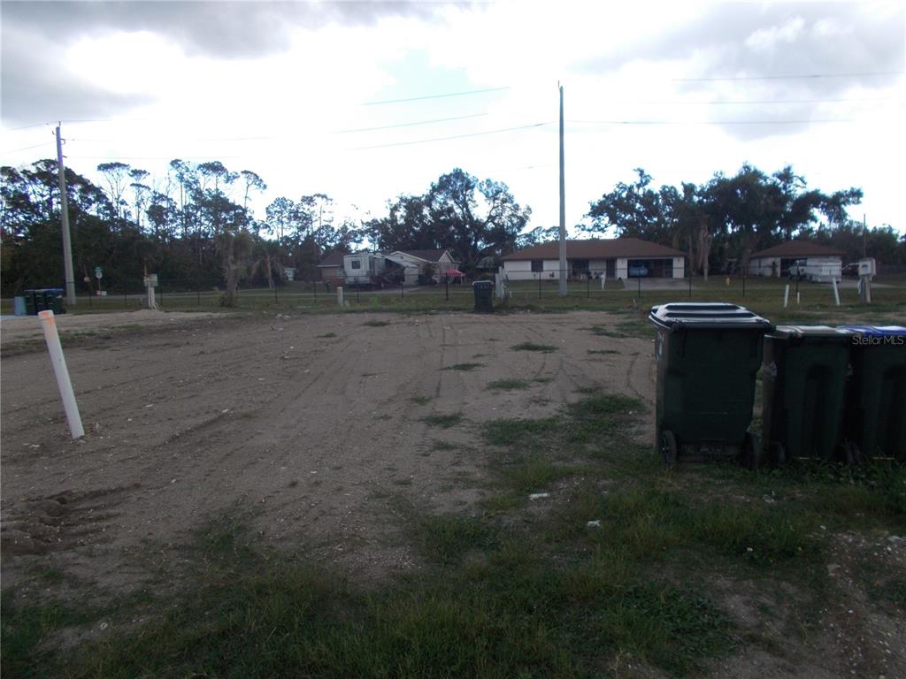 A vacant, dirt-covered residential lot features a white utility pipe and two trash bins — 5098 PALENA BOULEVARD, NORTH PORT, FL