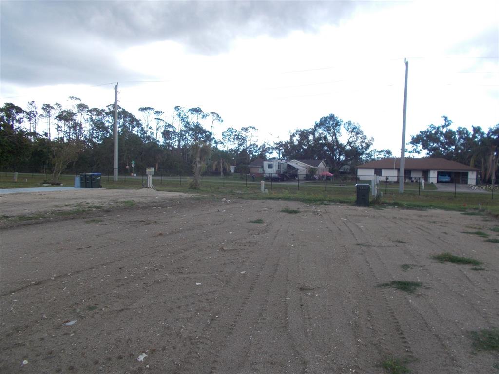 A vacant, sandy lot with tire tracks sits in front of a fenced residential area — 5098 PALENA BOULEVARD, NORTH PORT, FL