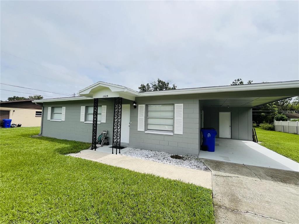 A single-story gray concrete block house features a front porch, carport, and white shutters — 1509 PHYLLIS STREET, LAKELAND, FL