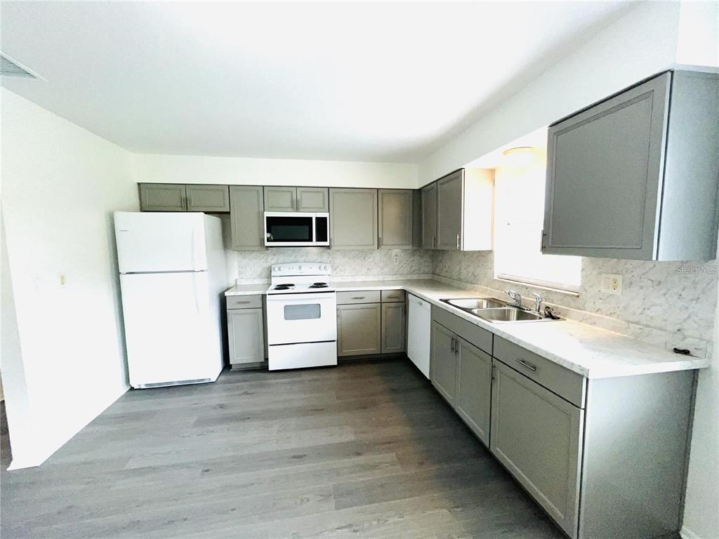 A kitchen features gray cabinets, white appliances, marble-look countertops, and light wood-look flooring — 1509 PHYLLIS STREET, LAKELAND, FL