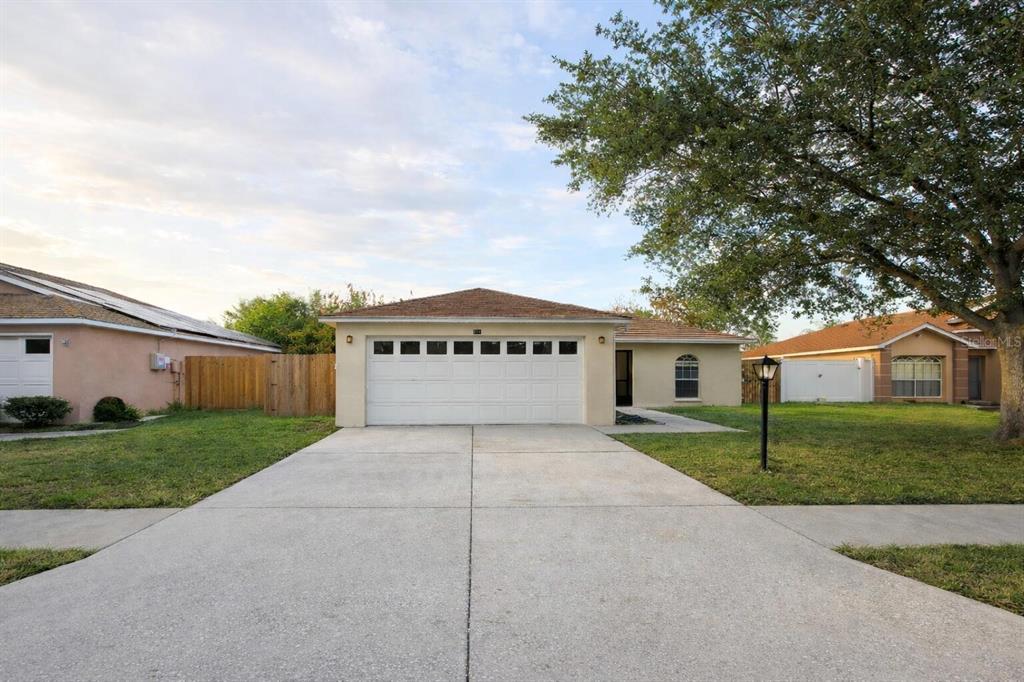 A single-story house with a white garage door, concrete driveway, and a large front tree — 101 DIAMOND RIDGE BOULEVARD, AUBURNDALE, FL