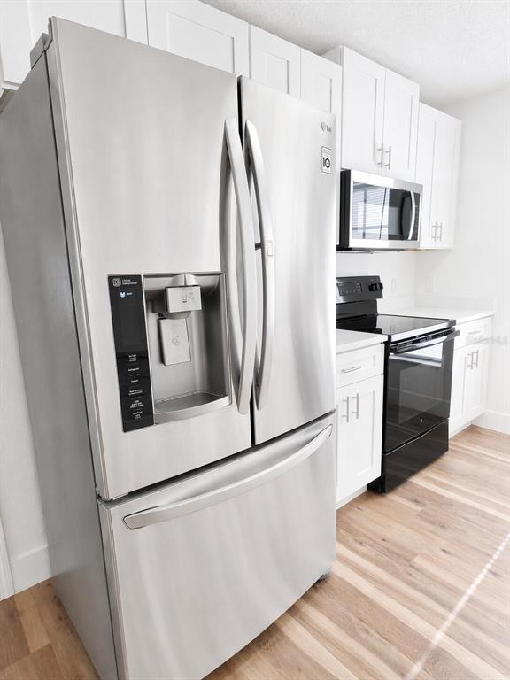 A kitchen features a stainless steel refrigerator, a black oven, and white cabinetry — 101 DIAMOND RIDGE BOULEVARD, AUBURNDALE, FL