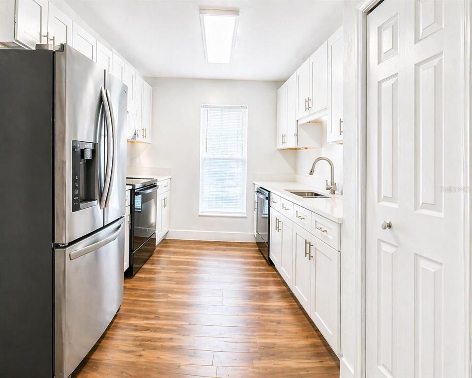 A galley kitchen features white cabinets, stainless steel appliances, and wood-look flooring — 101 DIAMOND RIDGE BOULEVARD, AUBURNDALE, FL