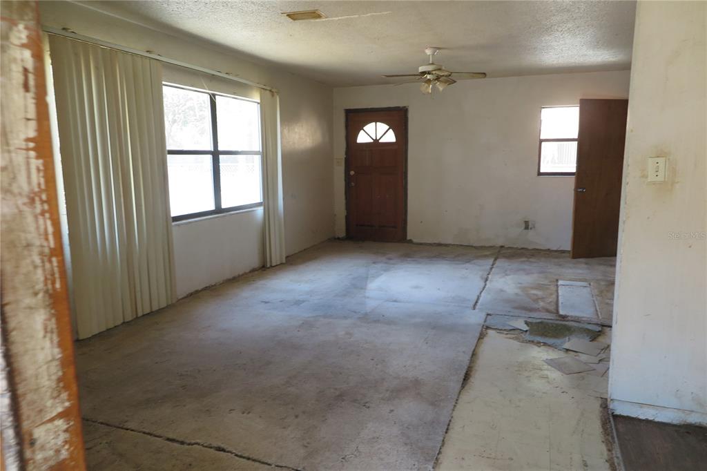 An unfurnished living room features a ceiling fan, a wooden front door, and worn flooring — 1045 SE 19TH STREET, GAINESVILLE, FL