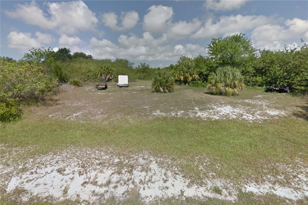 A vacant, grassy lot with scattered palm trees and two trailers under a cloudy sky — 9287 SNAPPER CIRCLE, PORT CHARLOTTE, FL