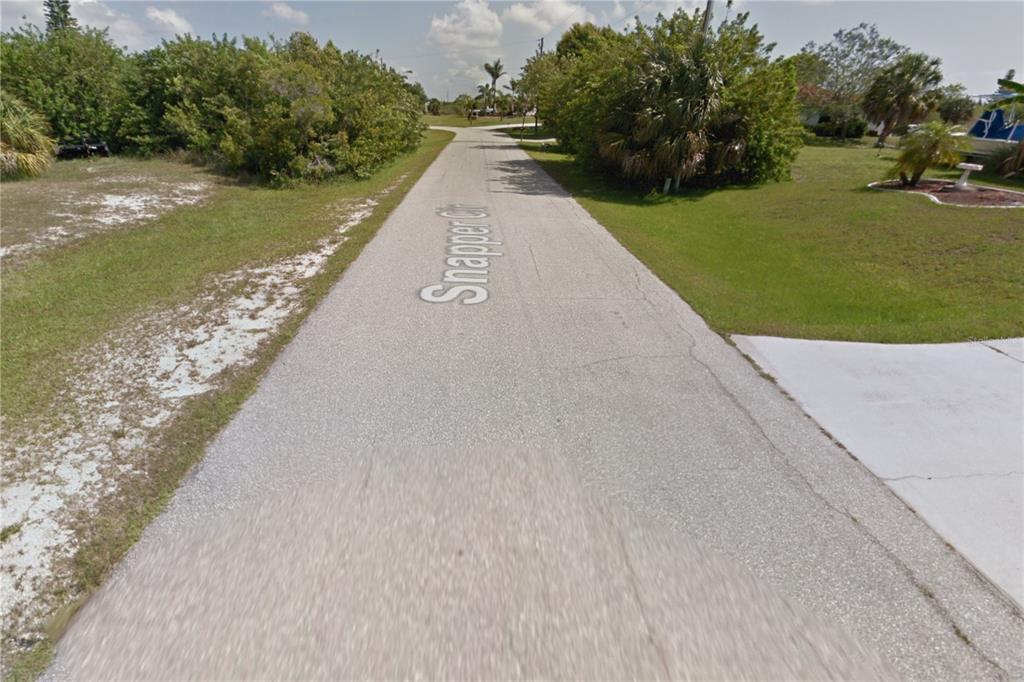 A paved residential street named Snapper Cir is lined with trees and grassy lots — 9287 SNAPPER CIRCLE, PORT CHARLOTTE, FL