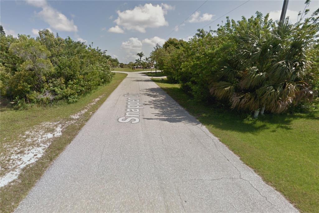 A paved road leads toward a T-intersection surrounded by dense trees and green vegetation — 9287 SNAPPER CIRCLE, PORT CHARLOTTE, FL