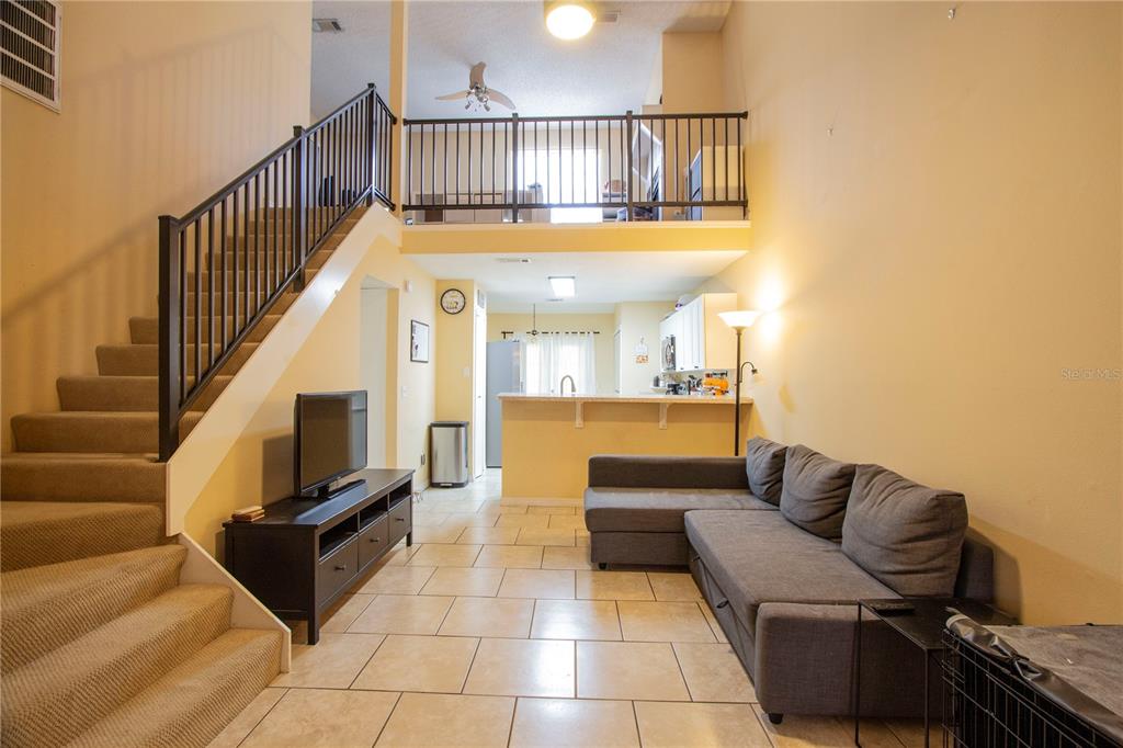 A living room with tile flooring, a staircase, and a loft overlooking the kitchen area — 12718 WOOD TRAIL BOULEVARD, TAMPA, FL