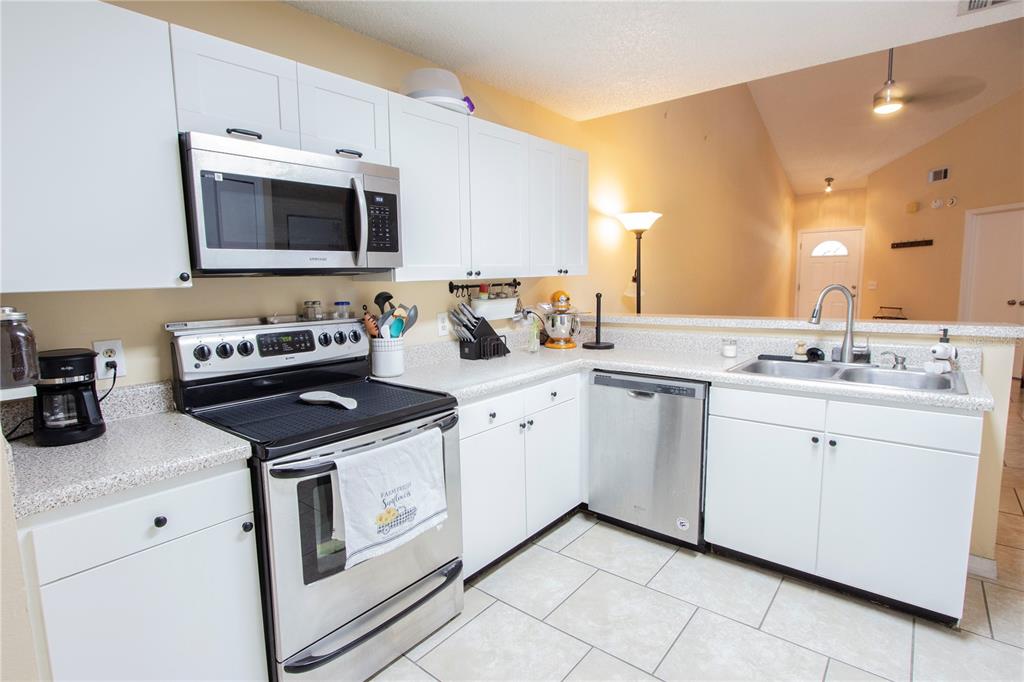 A kitchen features white cabinets, stainless steel appliances, and light-colored countertops — 12718 WOOD TRAIL BOULEVARD, TAMPA, FL