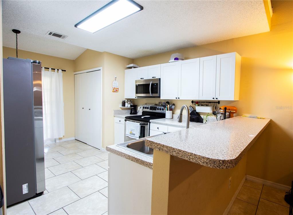 A kitchen features white cabinets, stainless steel appliances, a breakfast bar, and tile flooring — 12718 WOOD TRAIL BOULEVARD, TAMPA, FL