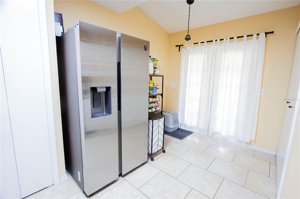A kitchen area features a stainless steel refrigerator, tile flooring, and sliding glass doors — 12718 WOOD TRAIL BOULEVARD, TAMPA, FL