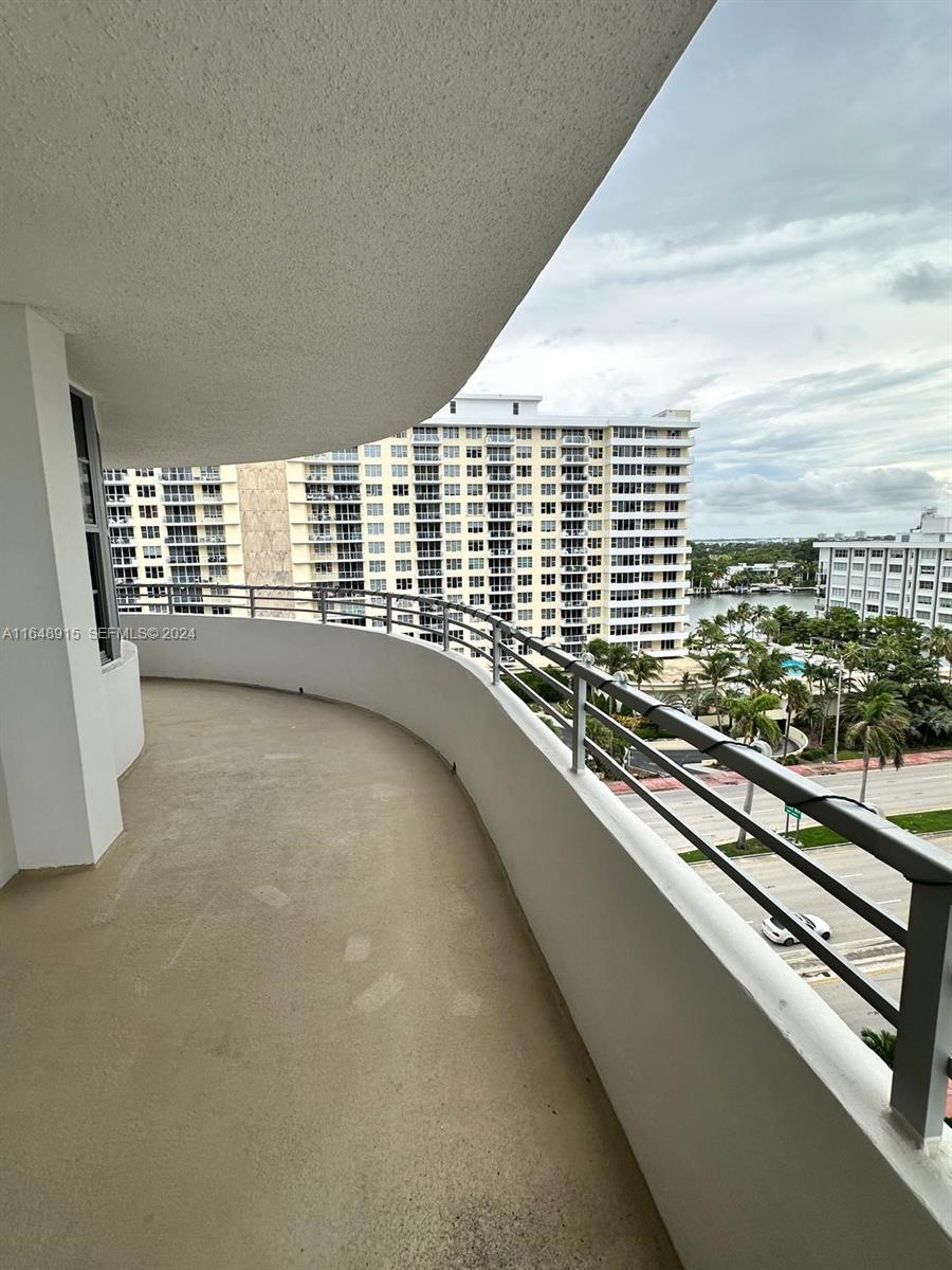 A curved balcony overlooks a street, palm trees, and a large residential building — 5555 Collins Ave # 10B, Miami Beach FL 33140, MIAMI BEACH, FL