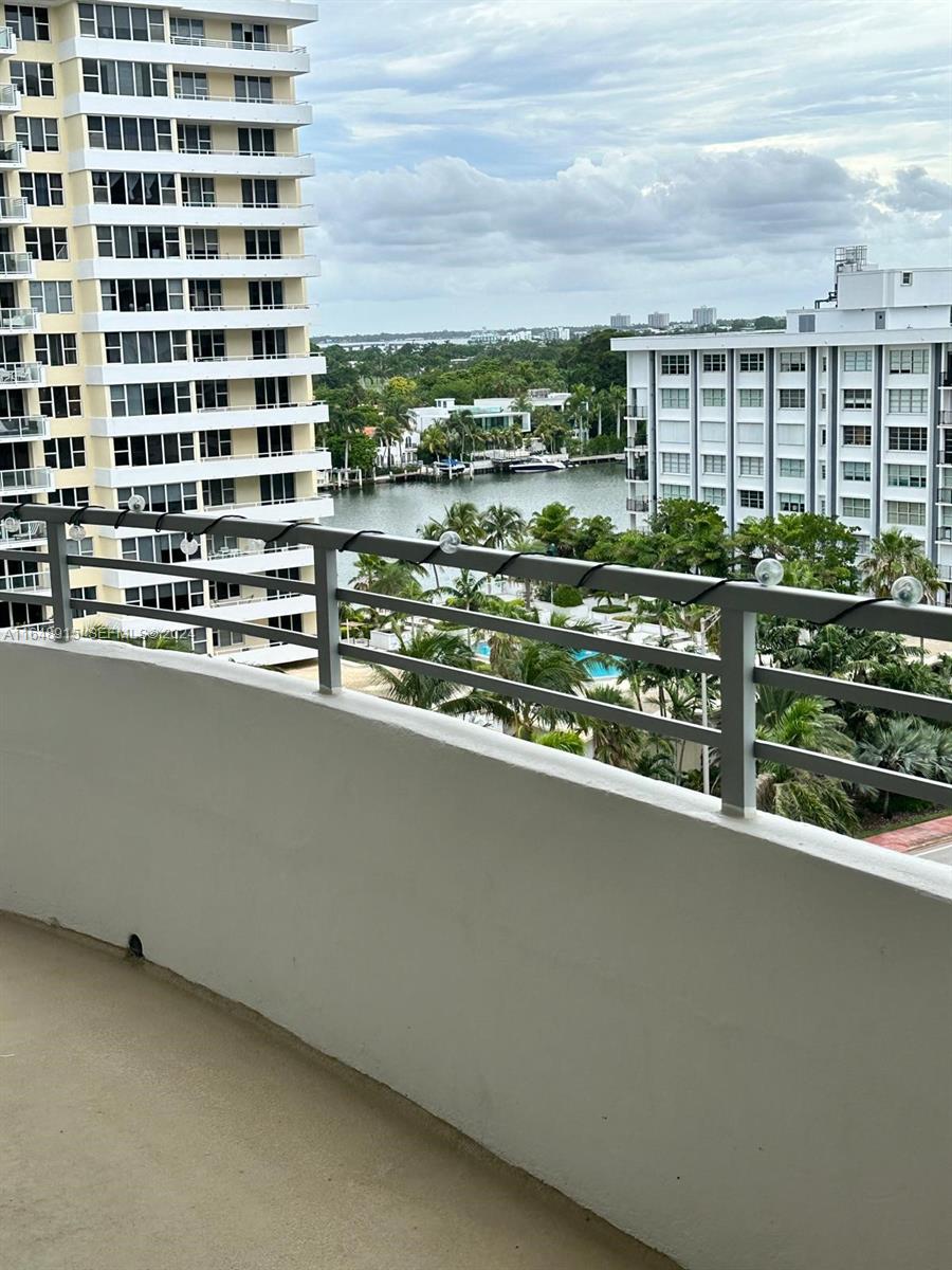 A balcony with a metal railing overlooks a waterway, palm trees, and nearby apartment buildings — 5555 Collins Ave # 10B, Miami Beach FL 33140, MIAMI BEACH, FL