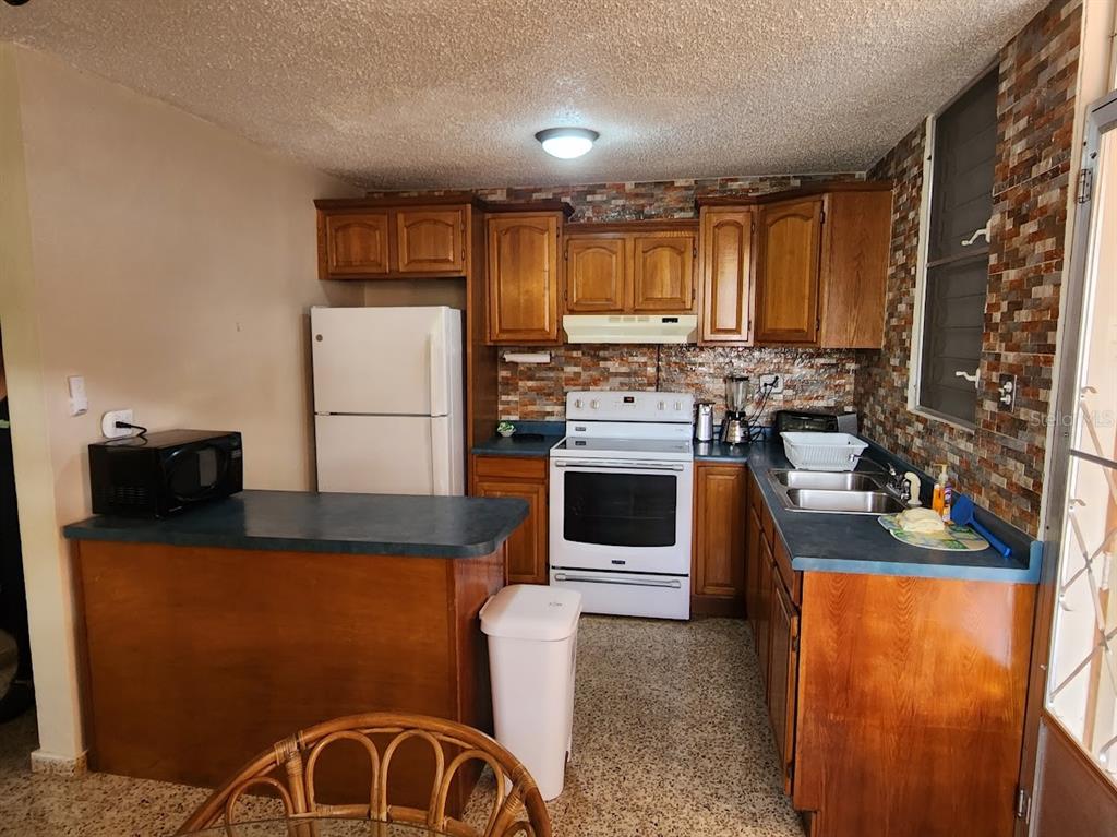 A kitchen features wood cabinets, a white refrigerator and stove, and a stone-tiled backsplash — 4-14 bloque 4k-10 ALTURAS DE MONTE BRISAS, FAJARDO, PR
