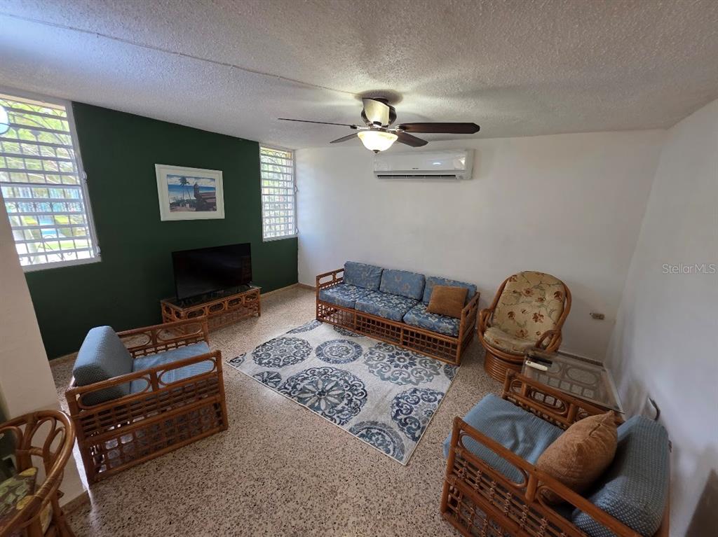 A living room features rattan furniture, a patterned area rug, and a green accent wall — 4-14 bloque 4k-10 ALTURAS DE MONTE BRISAS, FAJARDO, PR