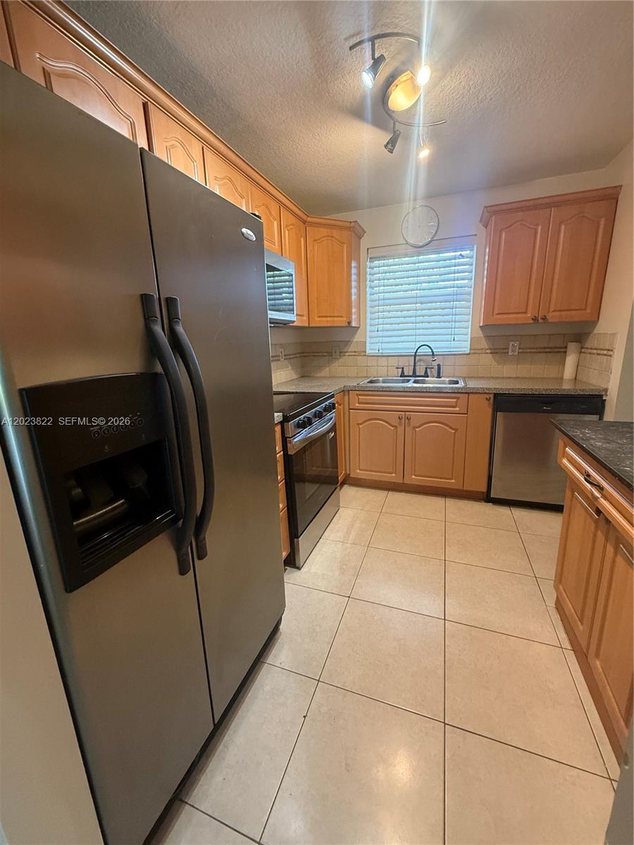 A kitchen features light wood cabinets, stainless steel appliances, and beige tile flooring — 5080 SW 64th Ave # 104, Davie FL 33314, DAVIE, FL