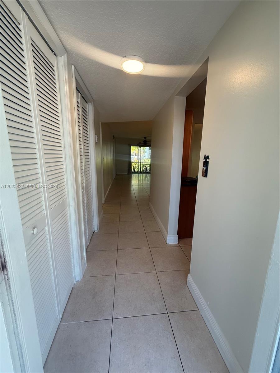 A hallway with light tile flooring leads toward a distant windowed doorway — 5080 SW 64th Ave # 104, Davie FL 33314, DAVIE, FL