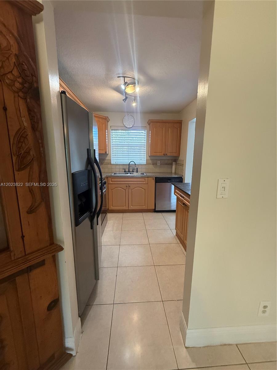 A galley-style kitchen features light wood cabinets, stainless steel appliances, and beige tile flooring — 5080 SW 64th Ave # 104, Davie FL 33314, DAVIE, FL